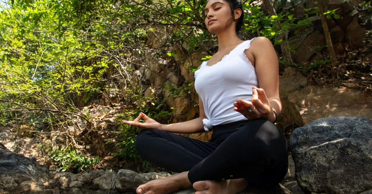 Jeune femme méditant au bord d'un ruisseau dans une forêt luxuriante, exsudant la tranquillité.