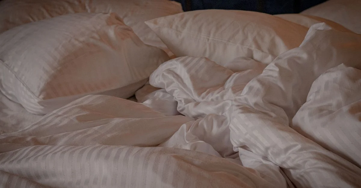 Un lit confortable et accueillant avec des oreillers blancs et une couette froissée, parfait pour une atmosphère relaxante.